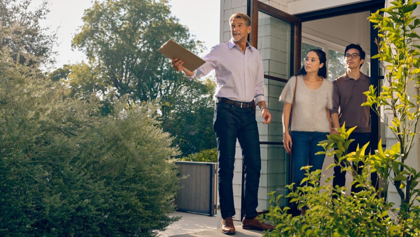 Real estate agent showing a house to buyers outside