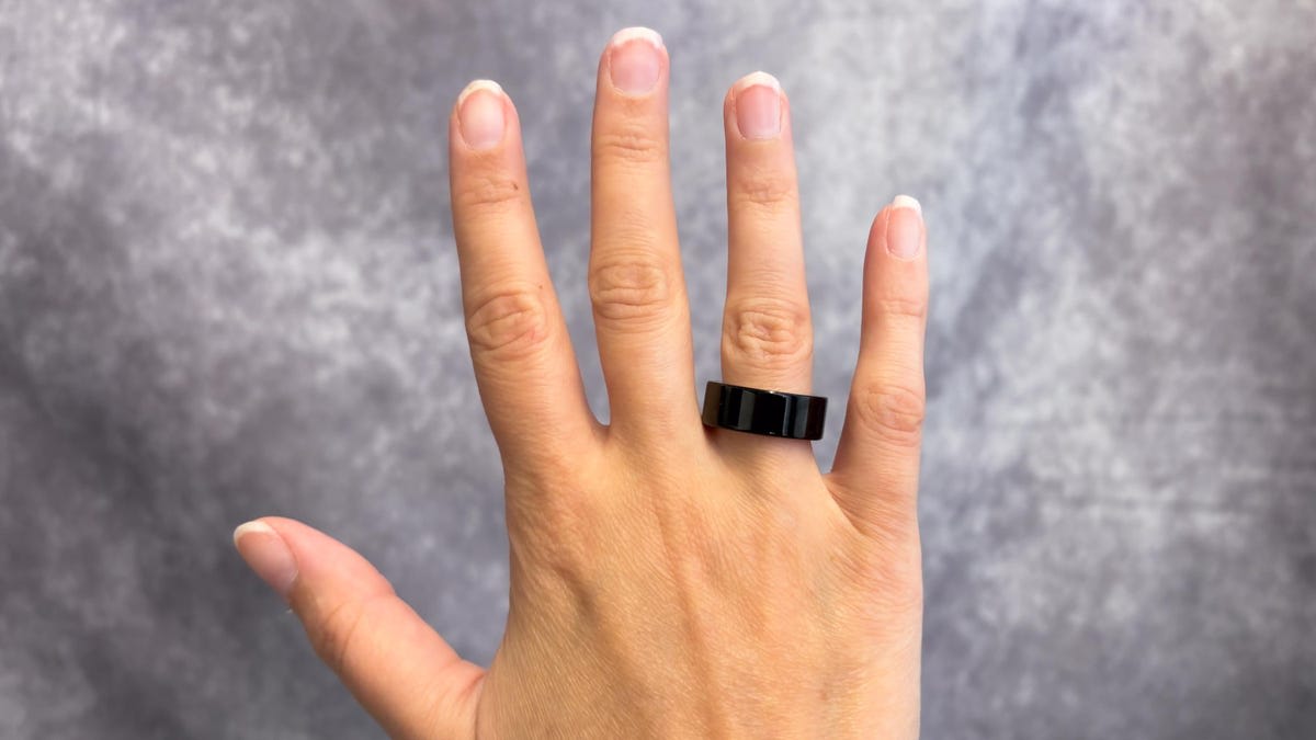 Oura Ring Gen 4 black titanium worn on finger close up against grey background