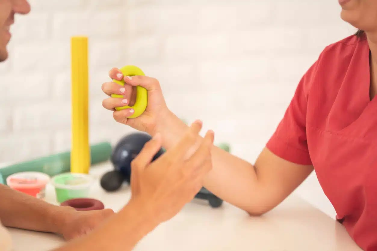 Fisioterapeuta auxiliando paciente em exercícios de reabilitação da mão com equipamentos de terapia