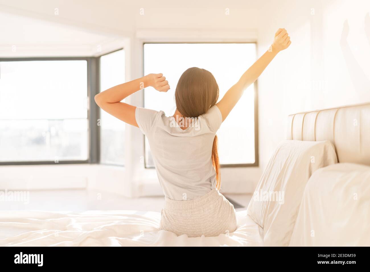 Woman waking up refreshed in a bright morning bedroom after following a cycle-aligned bedtime routine, stretching with natural light