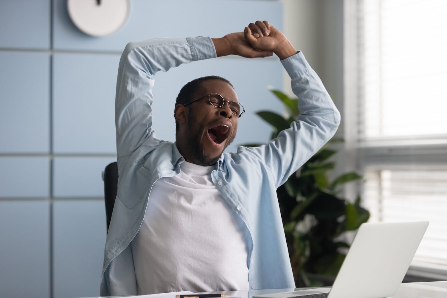 Man yawning at desk with laptop — sleep deprivation costs the US economy $411 billion per year