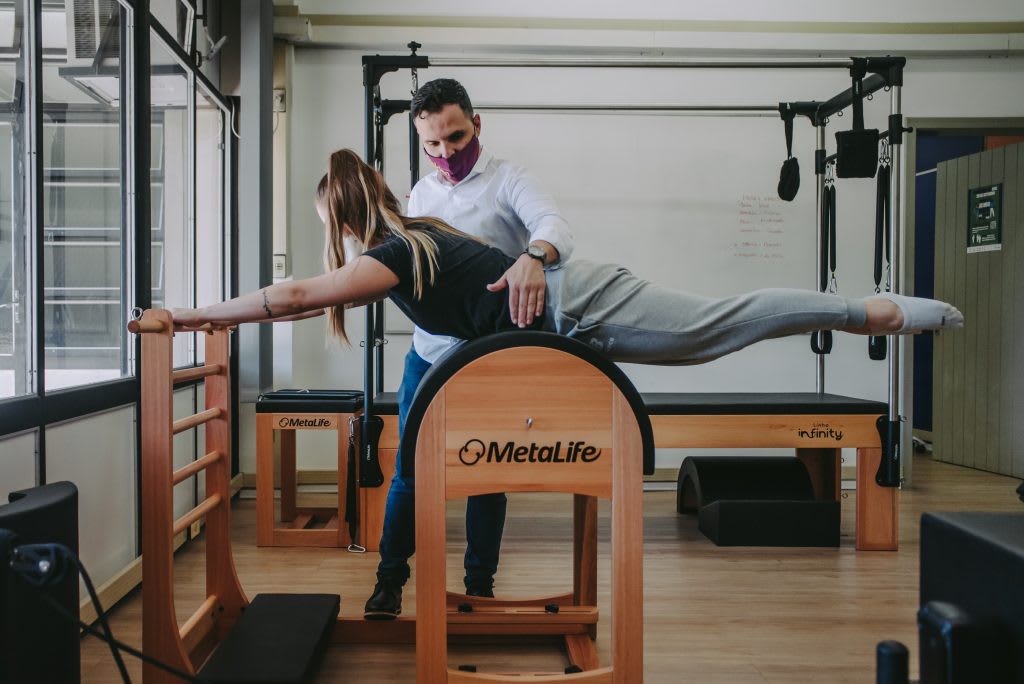 Fisioterapeuta auxiliando paciente em exercício de Pilates Clínico com equipamento especializado