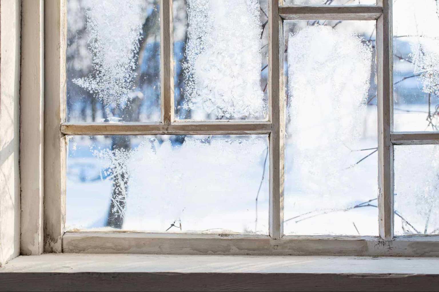 Thick frost buildup on a drafty wooden window frame indicating severe heat loss