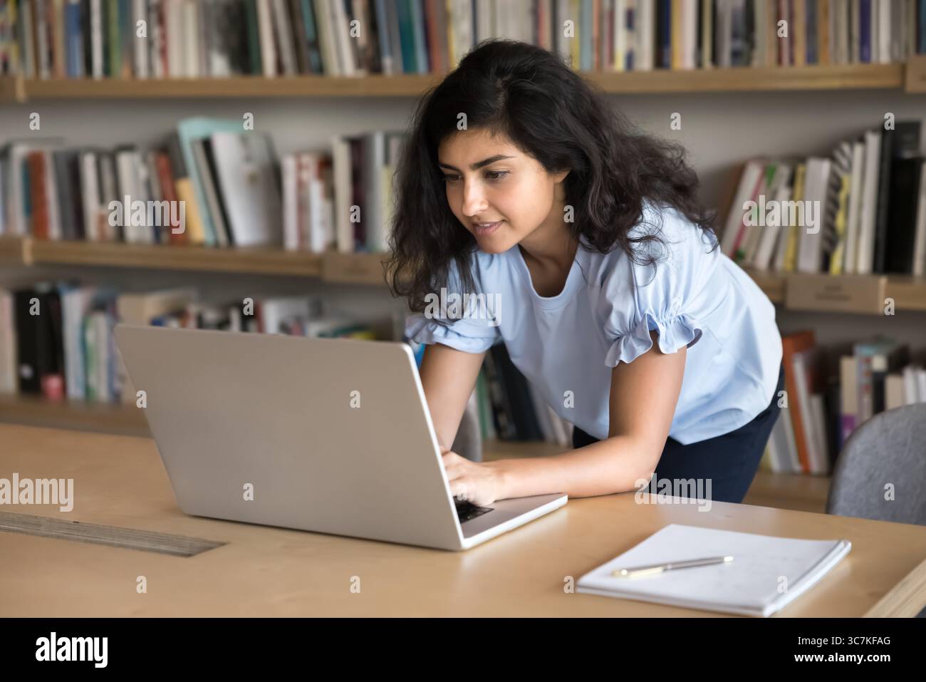 Indian student working on a laptop in a library, surrounded by books, representing online income and study balance.