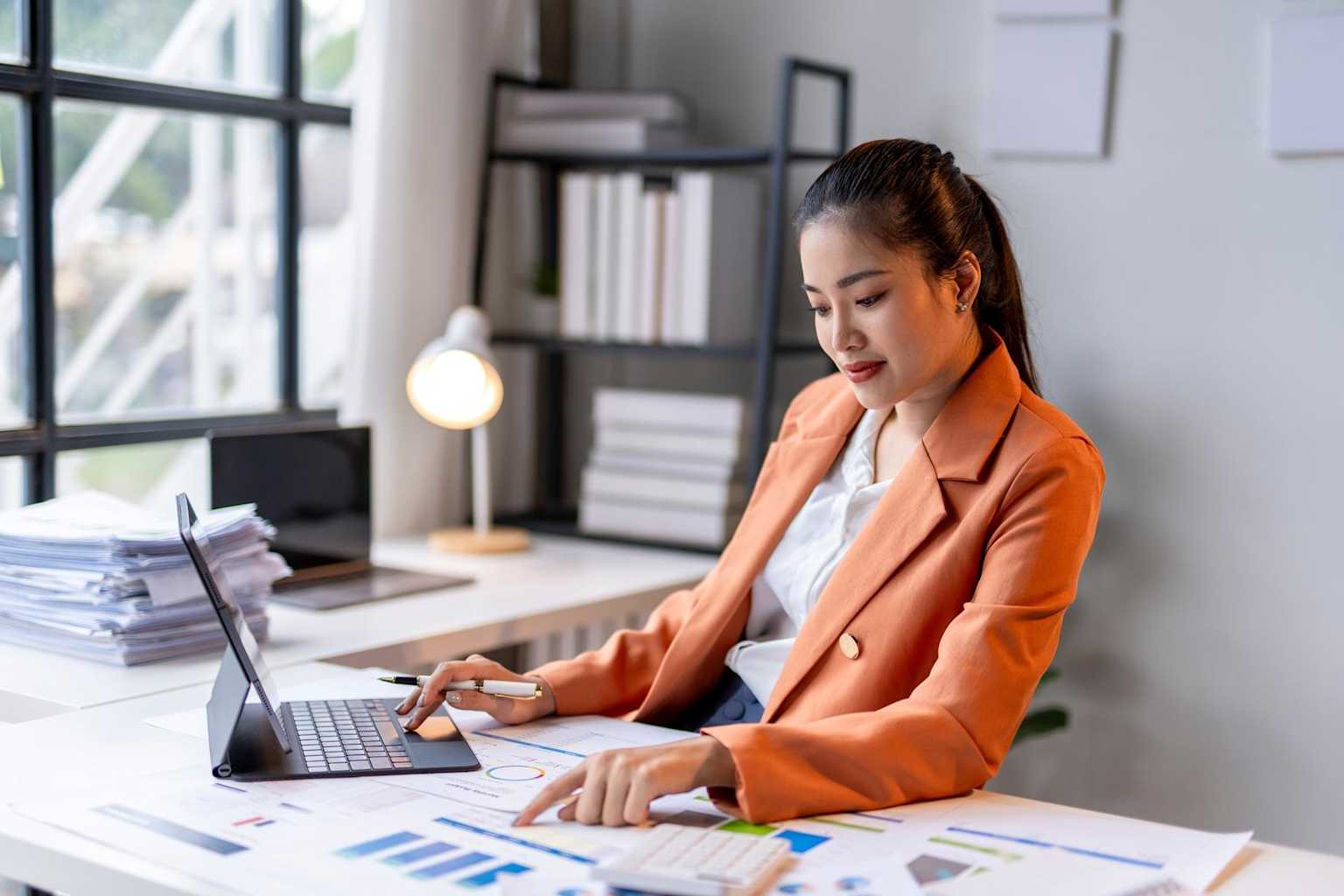 Une assistante comptable travaillant sur un ordinateur portable et des documents financiers dans un bureau professionnel