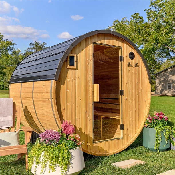 Outdoor cedar barrel sauna with open glass door on a green lawn with flower pots and trees in the background
