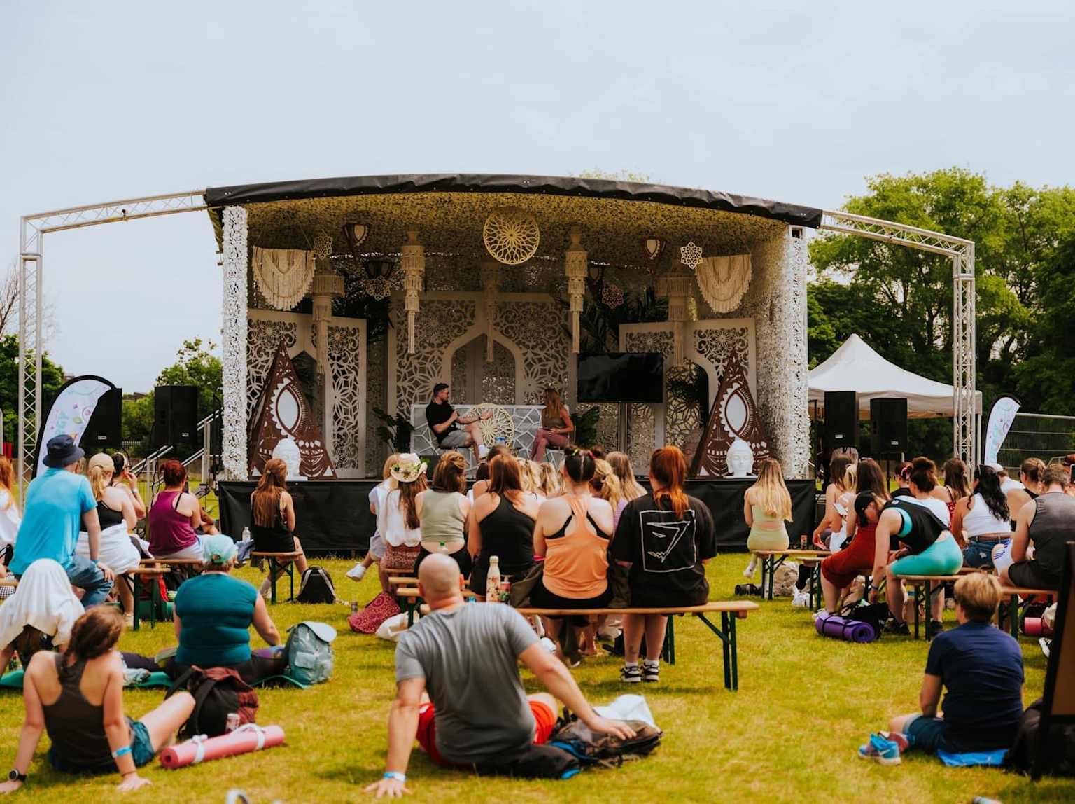 Outdoor wellness festival with performers and seated audience on grass