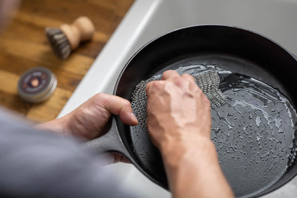 Scrubbing a cast iron skillet with a metal mesh pad under running water