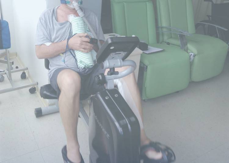 Idoso usando máscara de oxigênio e monitores, se exercitando em bicicleta estacionária em sala médica de reabilitação