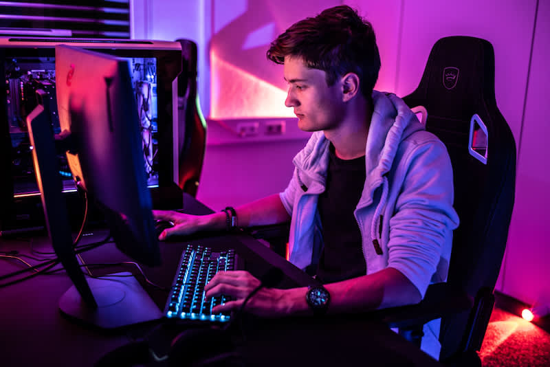Gamer seduto alla scrivania con setup gaming RGB e luci viola
