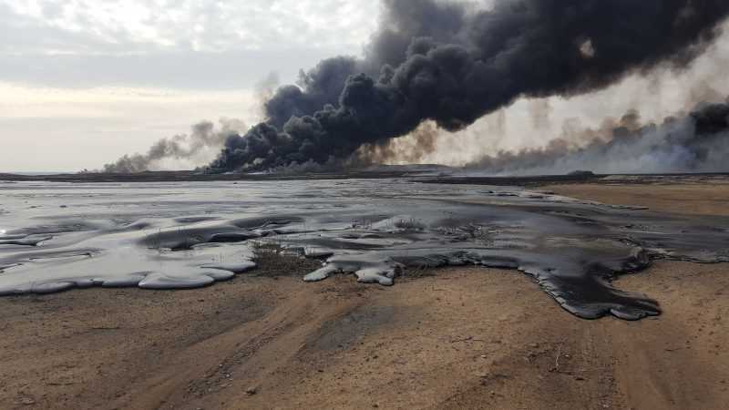 Oil fires burning with black smoke across a barren landscape