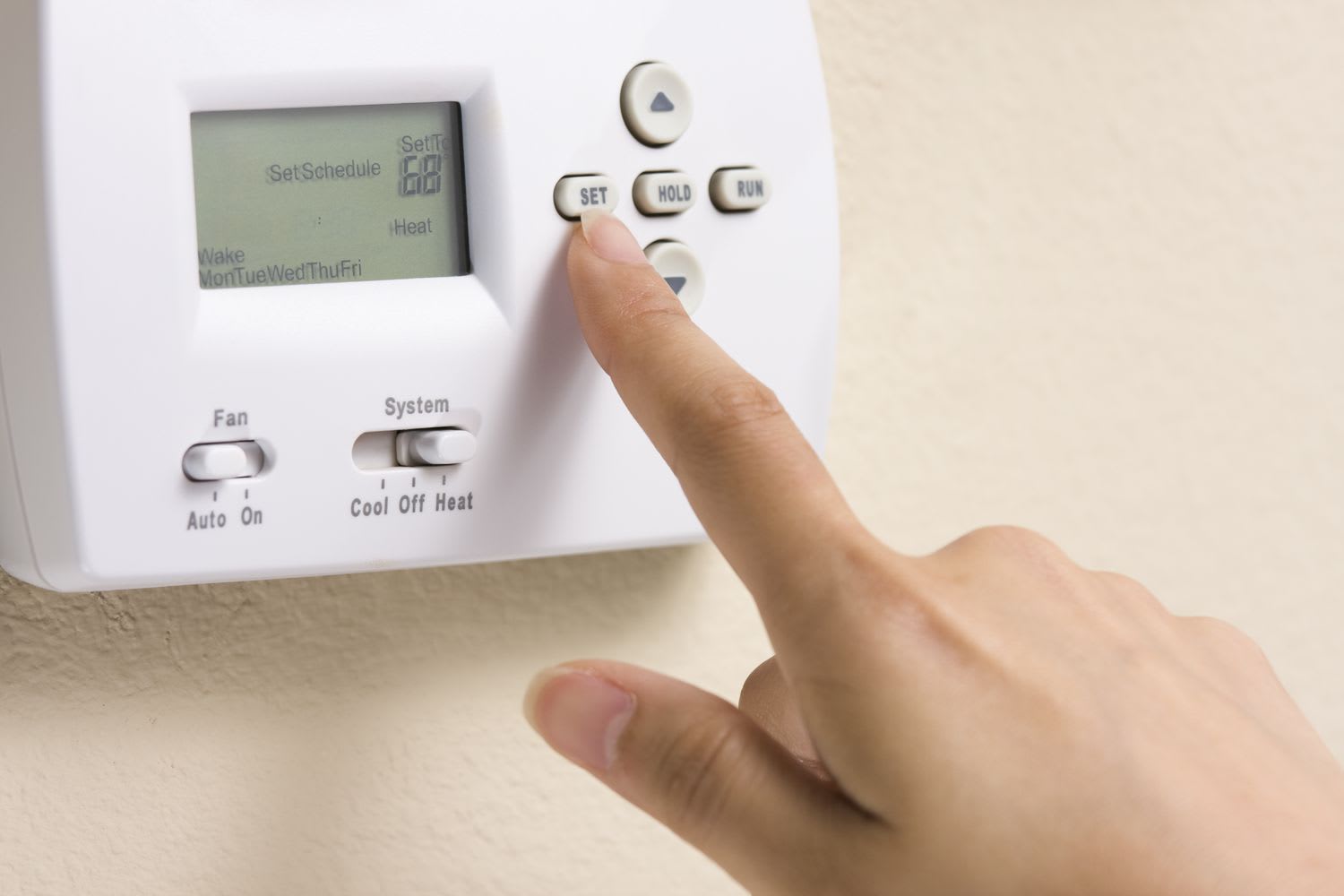 A hand manually adjusting a digital home thermostat to lower winter heating costs