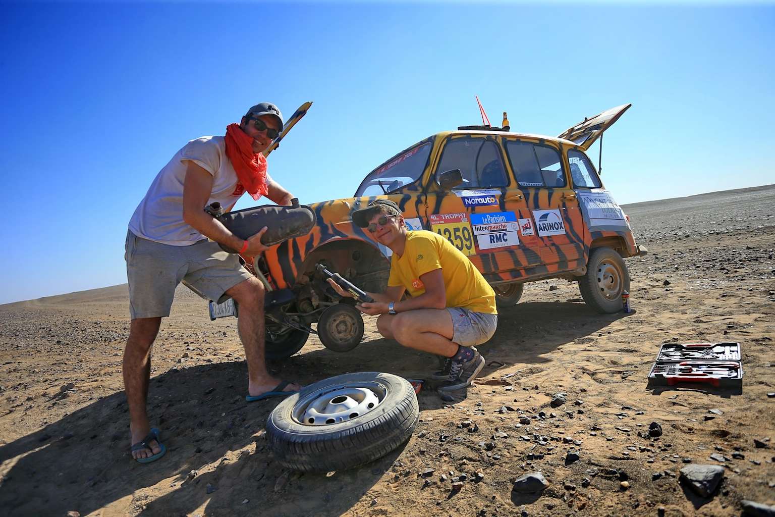 Deux personnes réparant un pneu sur leur 4x4 orange dans le désert