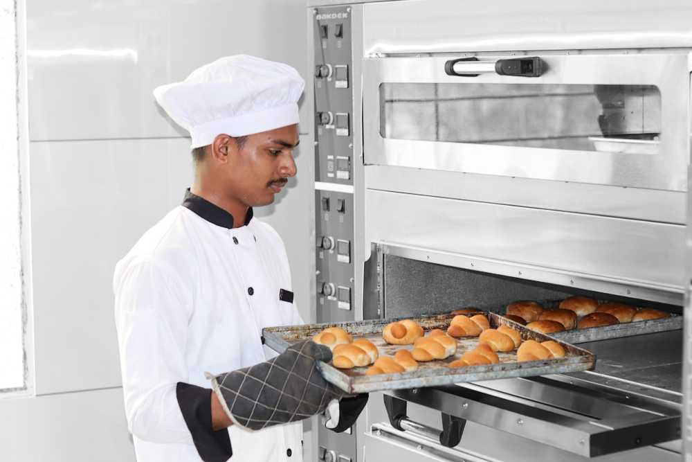 Baker pulling tray of freshly baked rolls from an oven