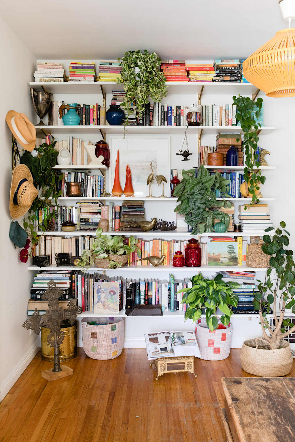 Bookshelf styled with books, plants, hats, and vases in eclectic arrangement