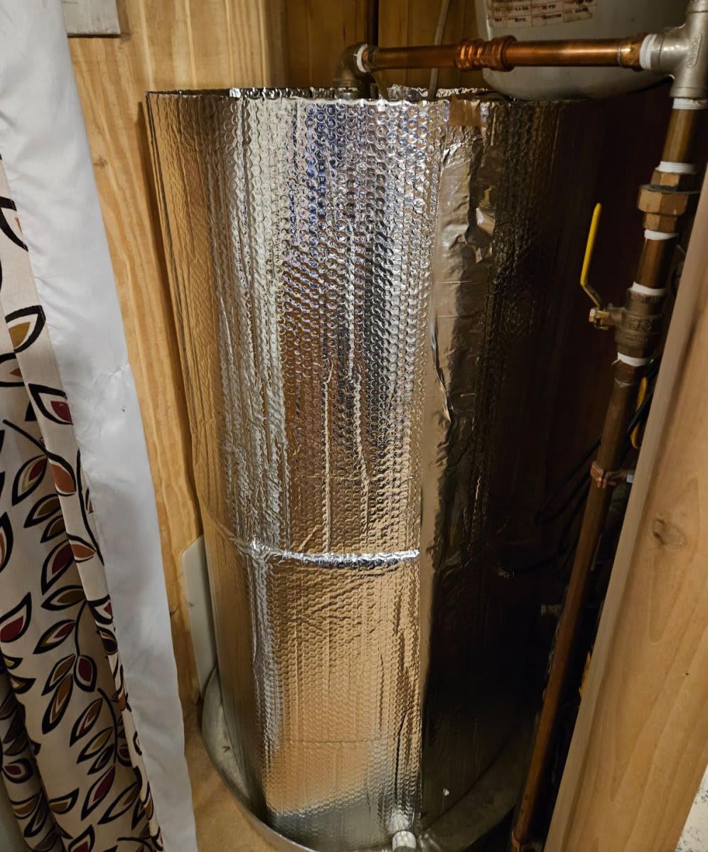 A water heater tank fully wrapped in a metallic foil insulation blanket