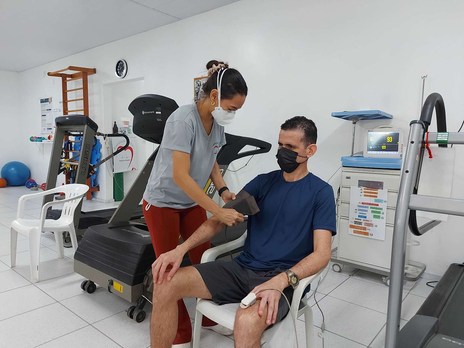 Profissional de saúde auxiliando paciente em exercício de reabilitação cardíaca em academia clínica