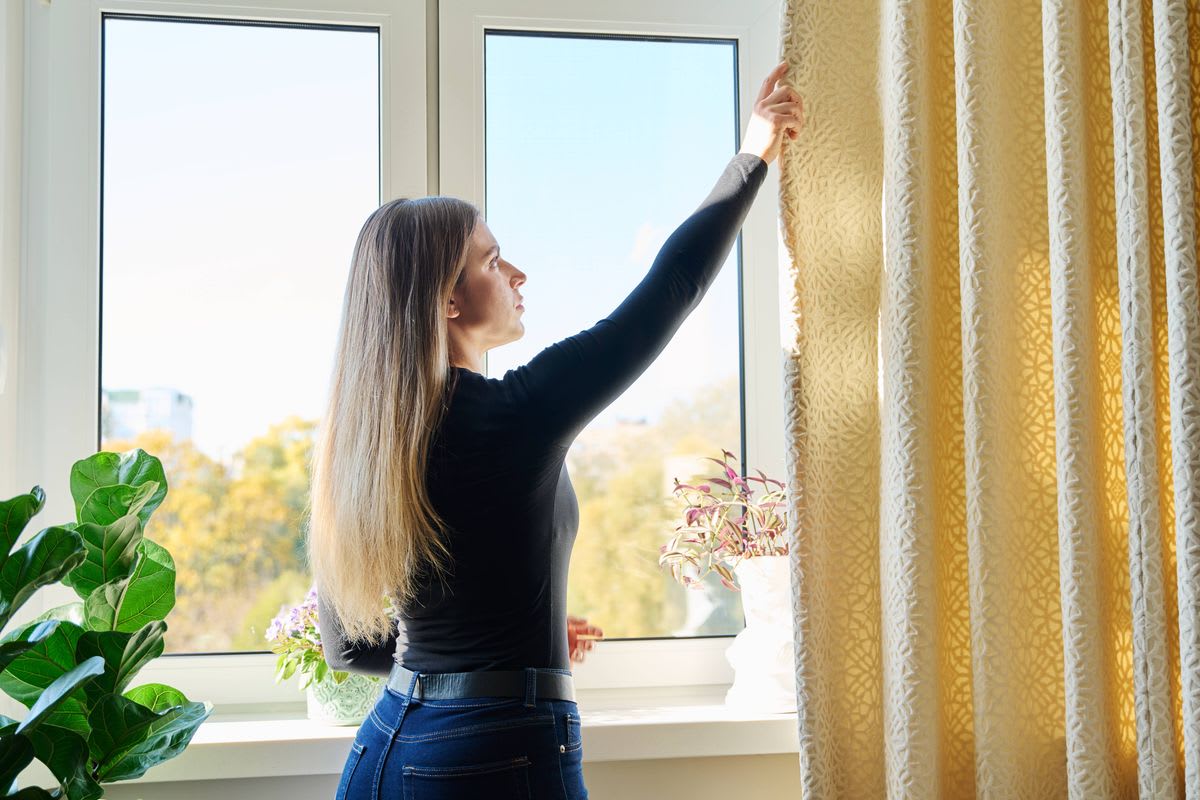 A homeowner opening curtains on a sunny winter day to harvest free solar heat