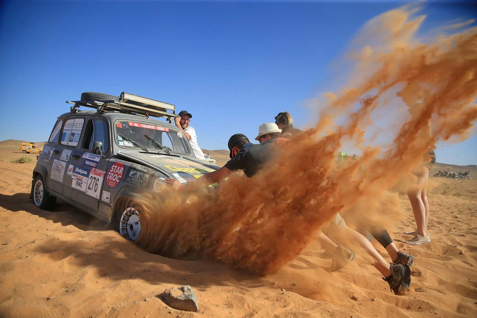 Participants poussant une voiture coincée dans les dunes de sable