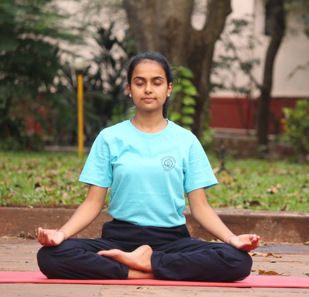Young Indian woman practicing lotus pose yoga meditation outdoors on red mat at Kaivalyadhama, Pune, eyes closed with hands in mudra position