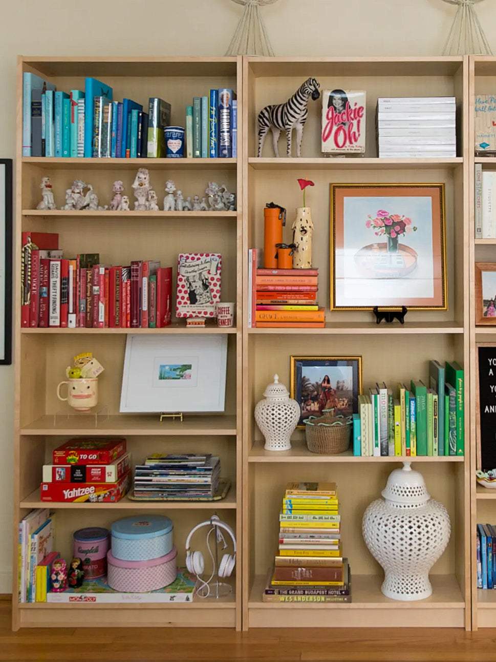 Styled bookcase with layered books of different heights, colorful spines, decorative objects, plants, and framed art