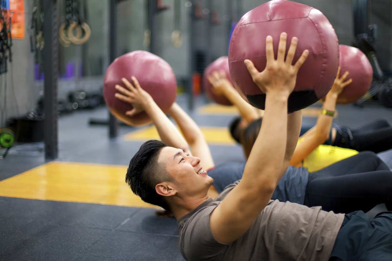 Grupo praticando exercícios anaeróbicos com bolas medicinais em academia