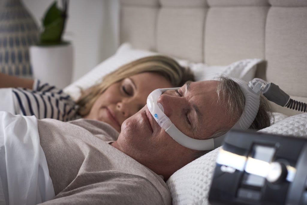 Couple sleeping with man wearing CPAP machine for sleep apnea treatment