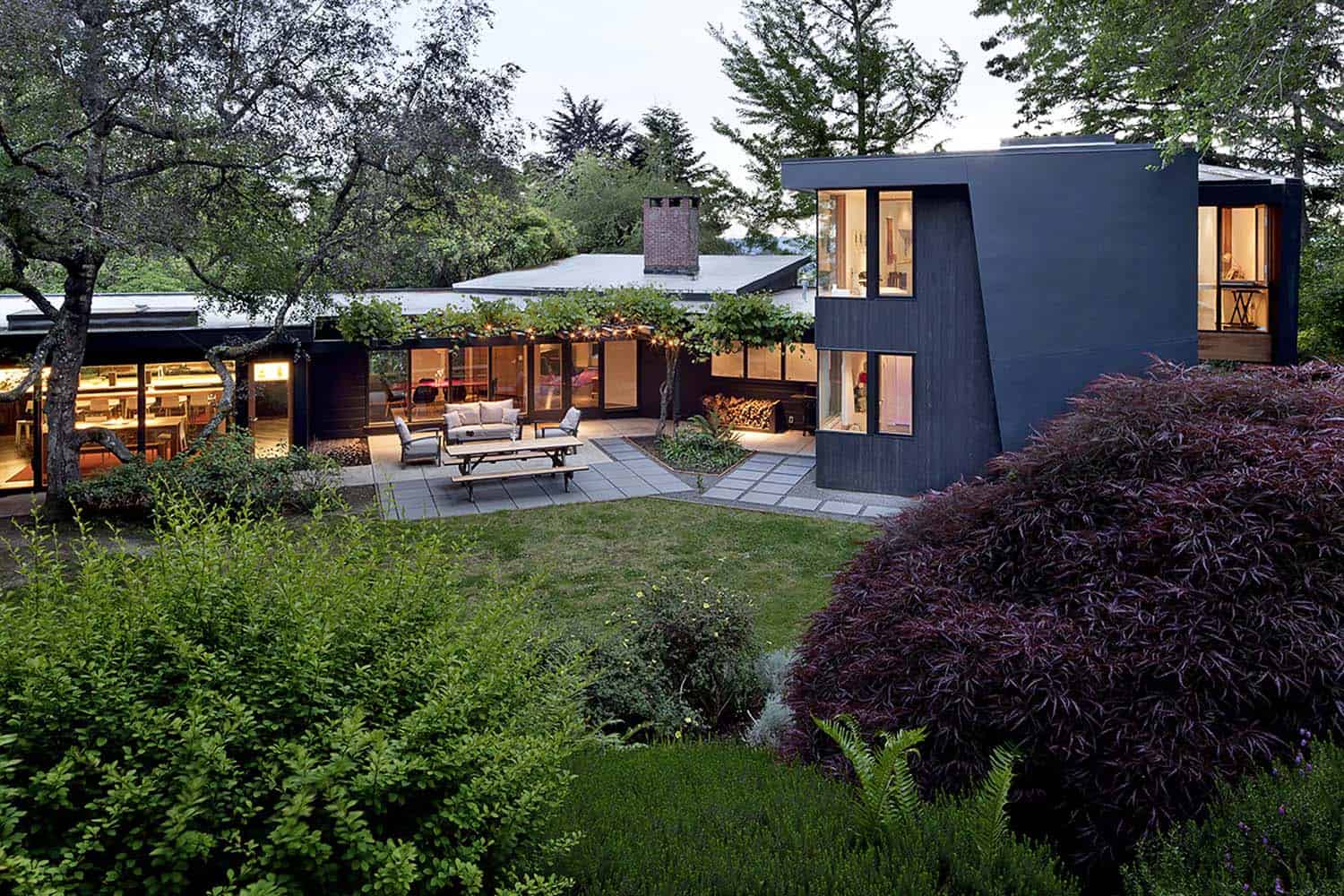 Mid-century modern home in Oregon's wooded hills with dark angular architecture and large glass windows at dusk