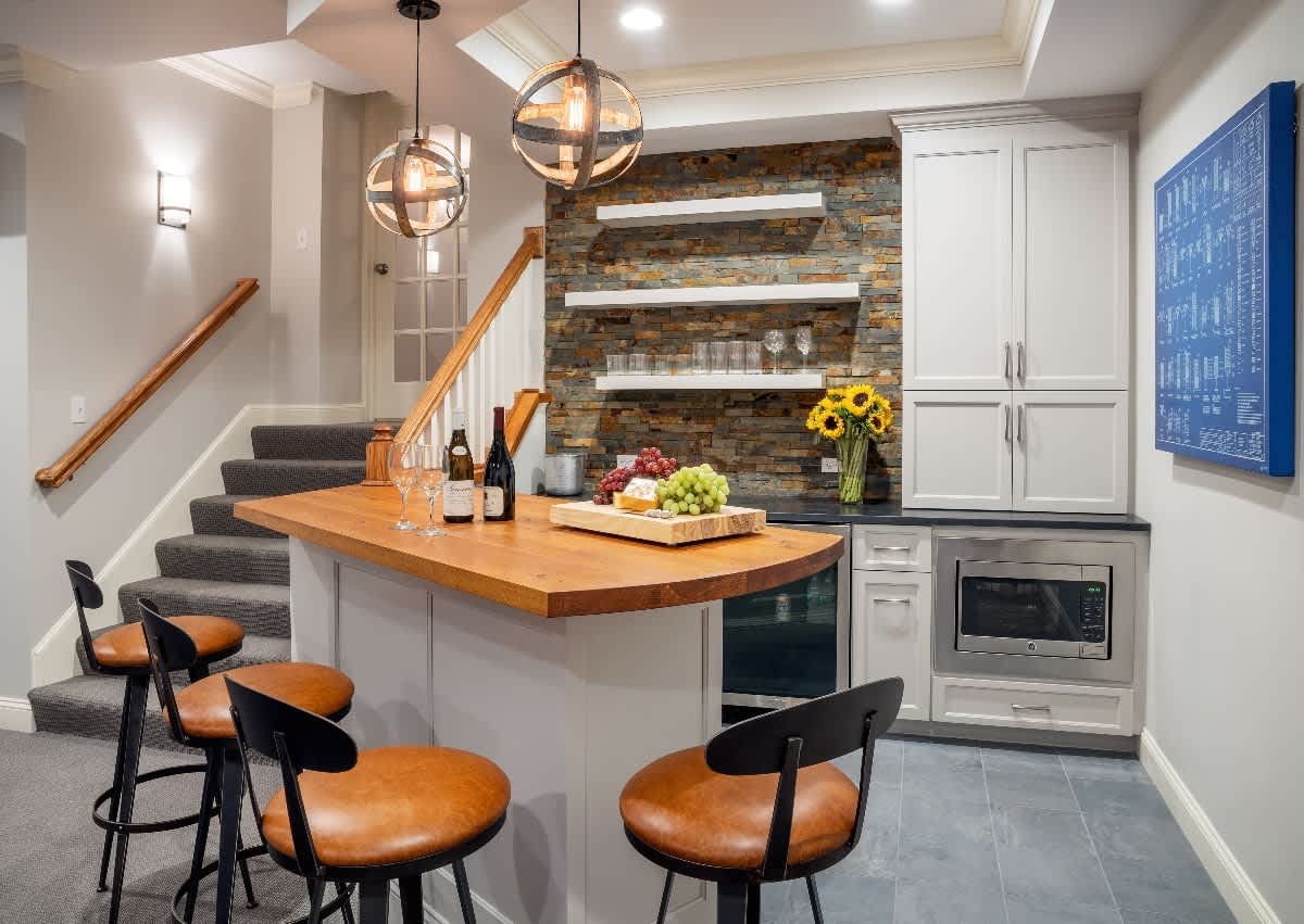 Modern basement bar with pendant lights, stone backsplash, bar stools, and kitchen island