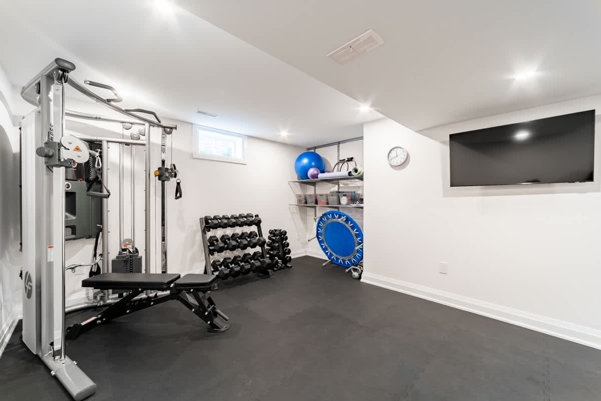 Renovated basement gym with exercise equipment, dumbbells, and wall-mounted TV