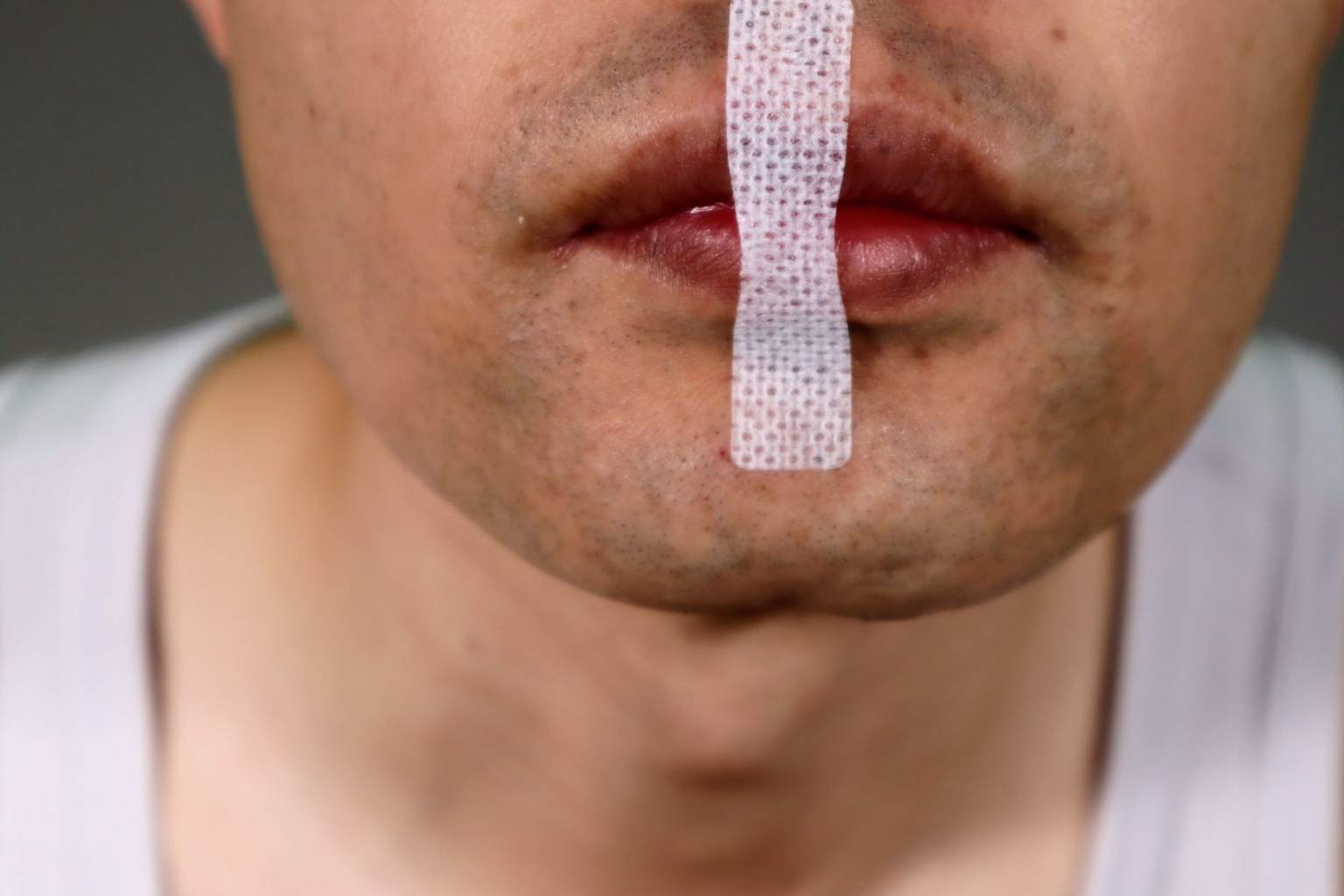 mouth taping for sleep safety — man with white medical tape applied over lips showing how mouth taping works at night