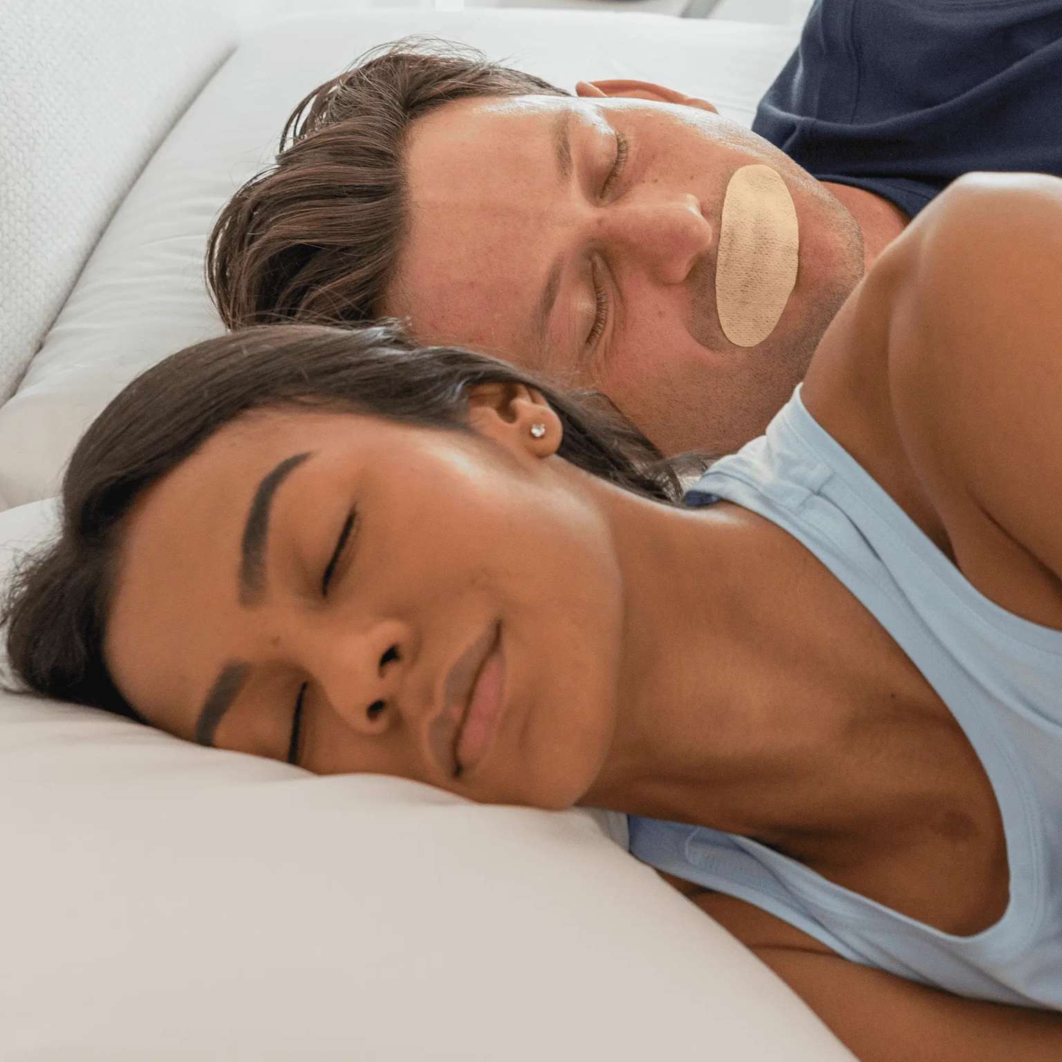 couple sleeping with mouth tape for snoring — man with beige tape strip showing viral sleepmaxxing snoring remedy that lacks RCT evidence