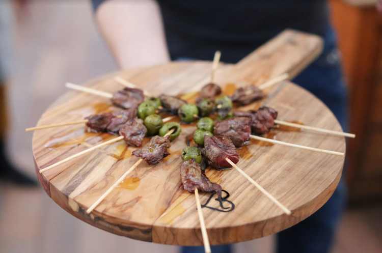 Spiedini di carne grigliata su tagliere di legno con erbe aromatiche