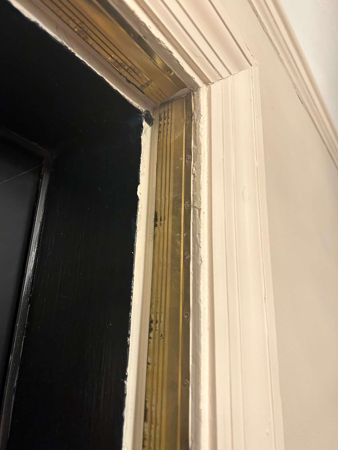 A homeowner using a tool to peel away old, crumbling weather stripping from a door jamb