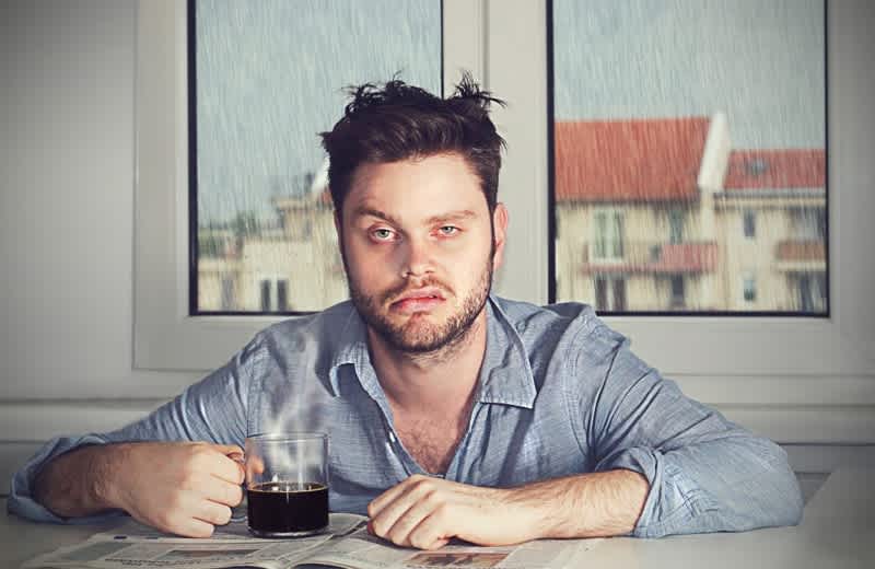 Man sitting at table holding coffee mug looking exhausted despite having slept 8 hours — illustrating non-restorative sleep