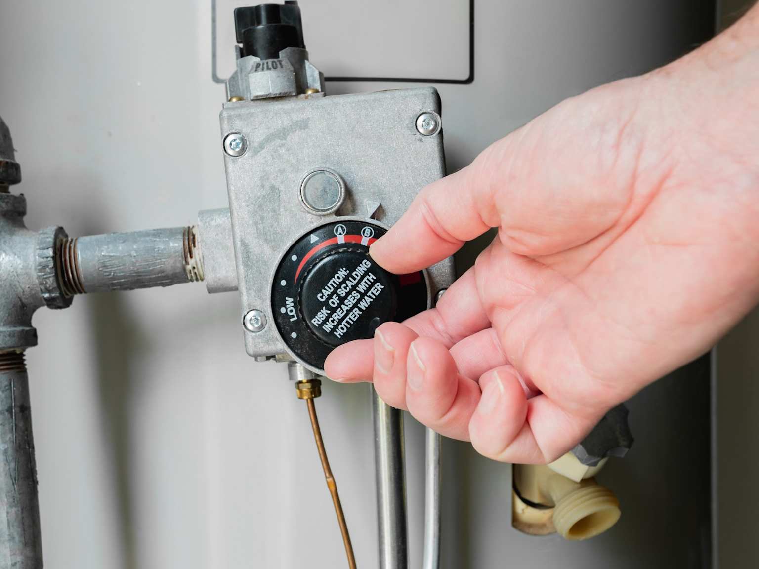 A homeowner manually adjusting their gas water heater thermostat dial down to 120 degrees