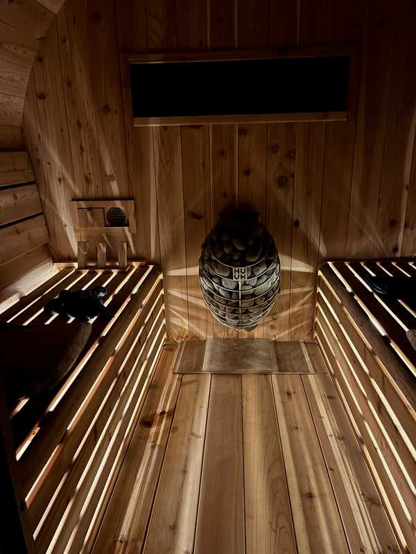 Barrel sauna interior showing curved cedar walls, tiered benches, and stone heater with warm ambient lighting
