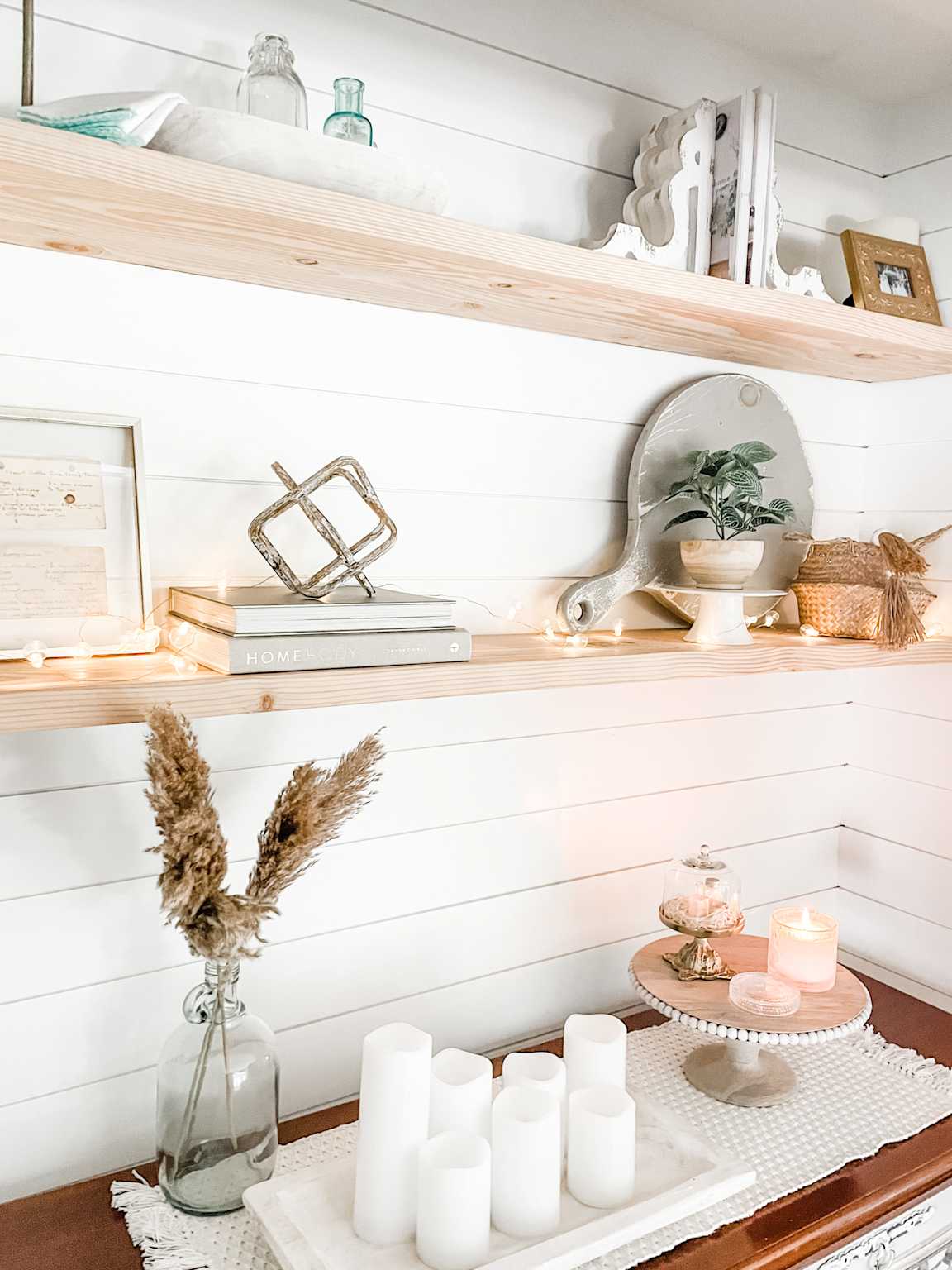Neutral floating wood shelves with books, candles, and plants on white shiplap wall