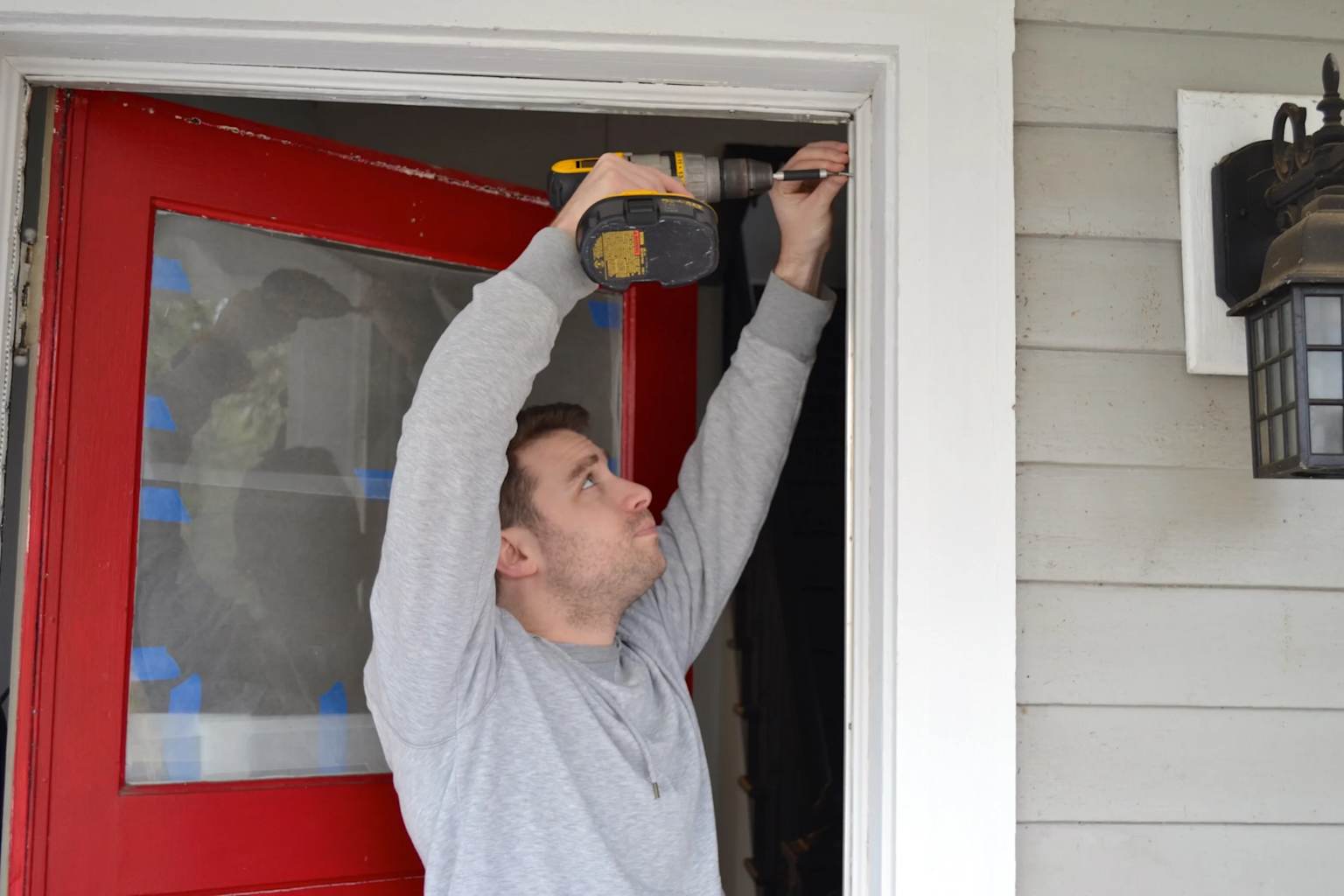 A person installing adhesive weatherstripping on a red door frame