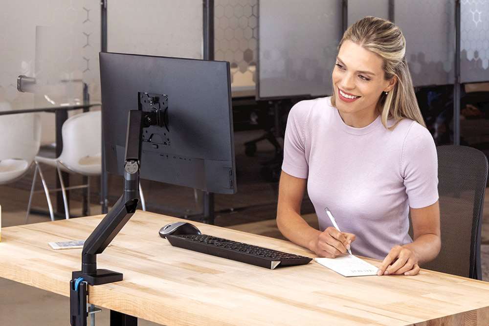 Woman working at a desk with an adjustable ergonomic monitor arm holding a large display at eye level