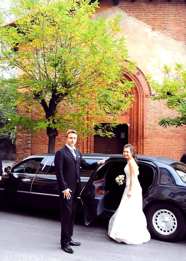 Bride and groom standing beside a luxury wedding limousine