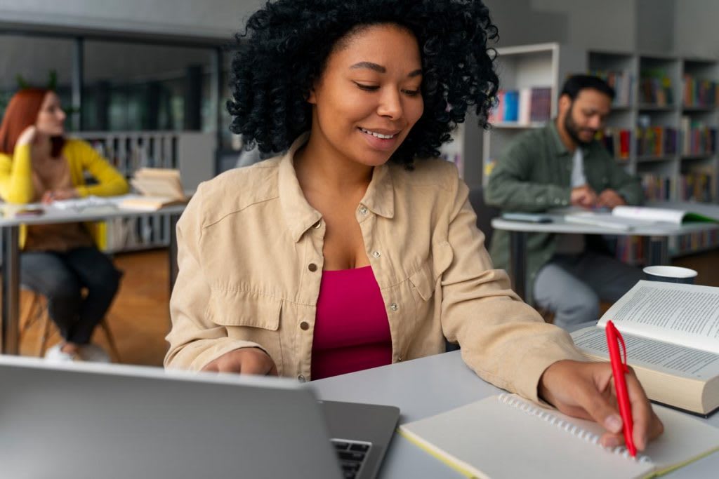 Une étudiante en formation comptabilité prenant des notes dans une bibliothèque, ordinateur ouvert devant elle