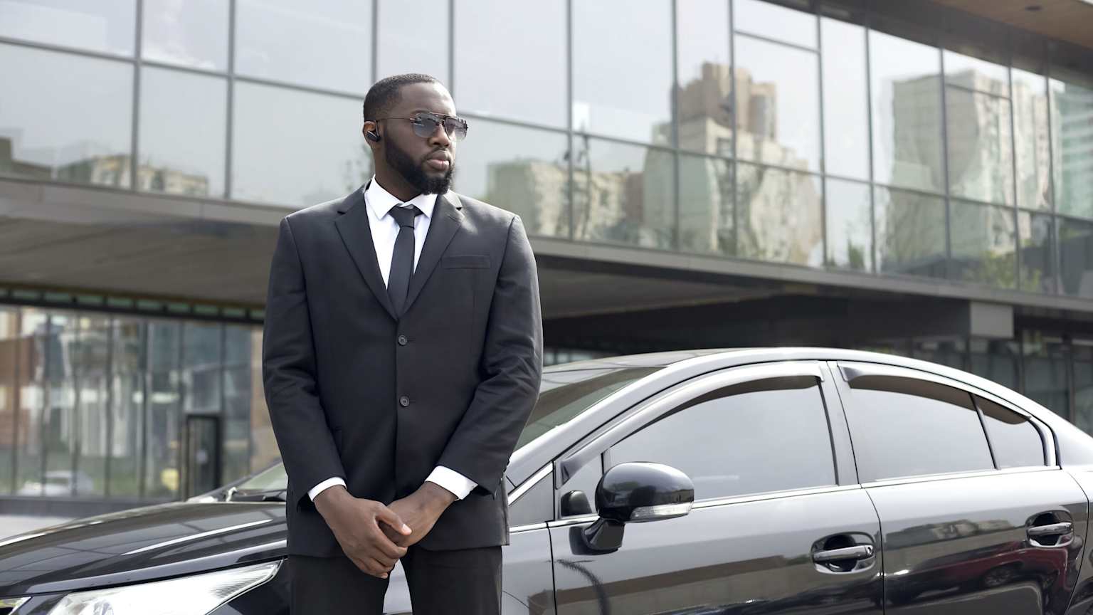 Executive protection officer beside black sedan