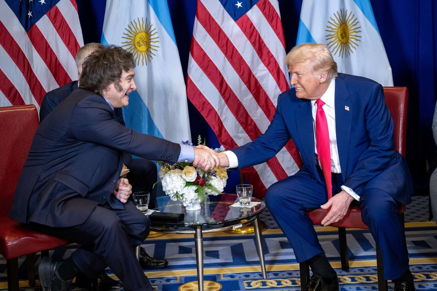 Milei y Trump apretón de manos con banderas argentina y estadounidense