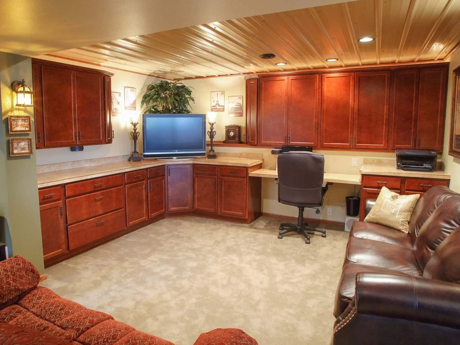 Finished basement home office with built-in wooden desk, cabinetry, and comfortable leather sofa