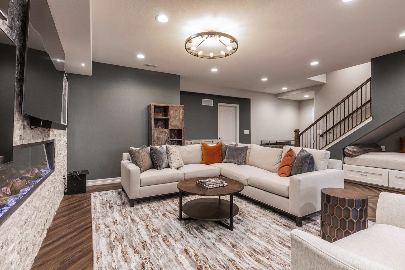 Modern finished basement with L-shaped sofa, gas fireplace, mounted TV, and built-in cabinets