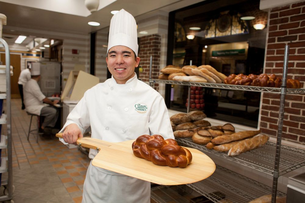 Professional baker holding fresh braided bread in a bakery kitchen