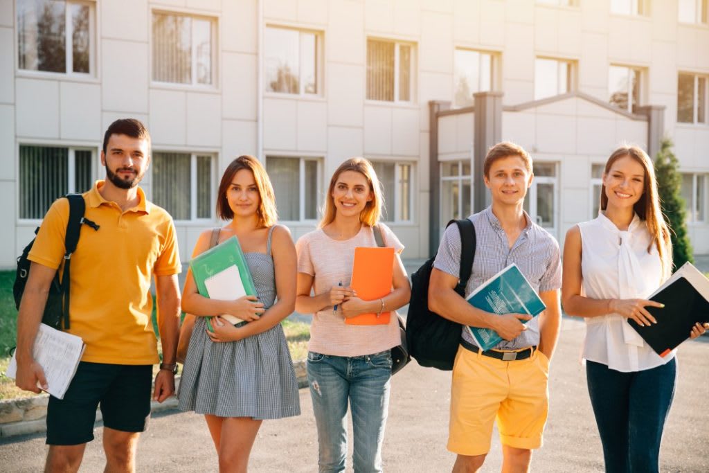 Międzynarodowi studenci z notatnikami przed nowoczesnym budynkiem uczelni w Polsce
