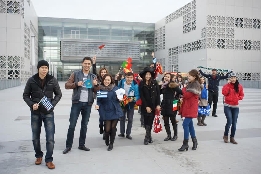 Międzynarodowi studenci z flagami przed nowoczesnym budynkiem uczelni