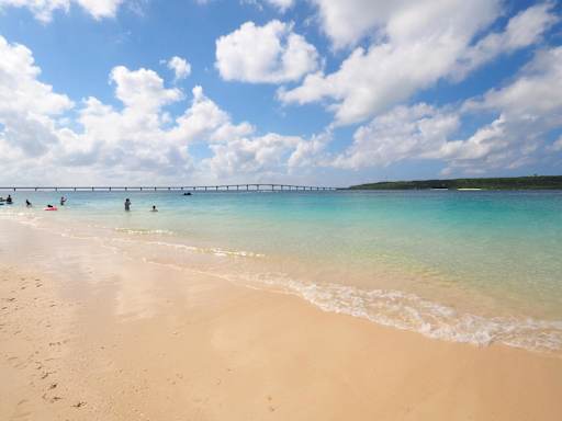 Yonaha Maehama beach on Miyako Island, featuring a long bridge stretching across the water towards a green landmass.